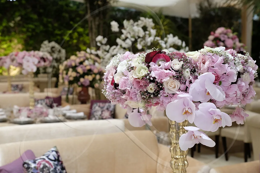 Pink floral centrepiece on gold stand with fine tableware in the background, Rahal Maître Traiteur